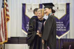 Girl in graduation cap and gown being presented with a diploma